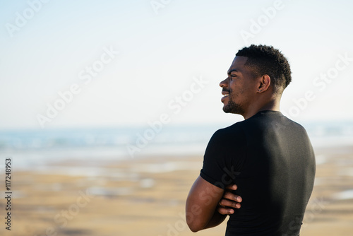 Running and healthy lifestyle success. Cheerful black man taking a workout rest at the beach. Motivation in sport concept.