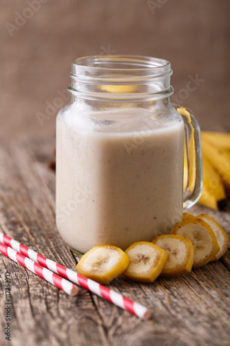 Healthy banana smoothie in glass jar with bananas on wooden tabl