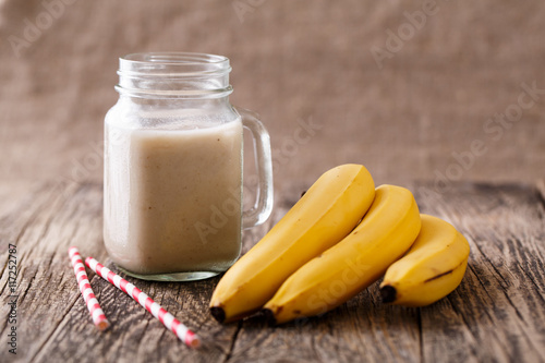 Healthy banana smoothie in glass jar with bananas on wooden tabl