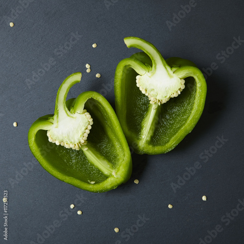 Green sweet bell pepper halves with a sharp kitchen knife on a rustic slate chopping board background