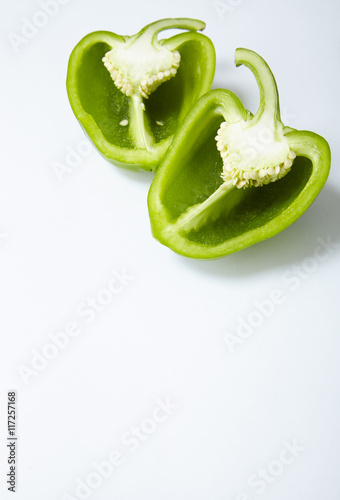 A green sweet bell pepper cut in half on an off white background forming a page border