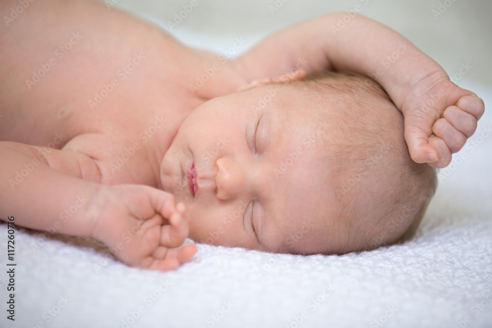 Portrait of young funny newborn babe napping on soft white knitted blanket with his arms up. Cute caucasian new born child sleeping. Healthy one month old kid lying on bed with closed eyes. Close-up Portrait of young funny newborn babe napping on soft white knitted blanket with his arms up. Cute caucasian new born child sleeping. Healthy one month old kid lying on bed with closed eyes. Close-up
