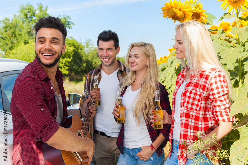 Young people listening guy playing guitar friends drinking beer bottles outdoor countryside