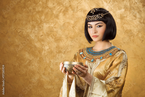 Beautiful woman like Egyptian Queen Cleopatra with cup on golden background photo