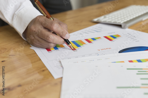 businessman hand holding pen with graph and chart analysis paper