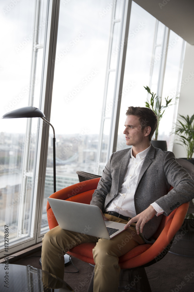 Businessman Sits In Chair With Laptop In High Rise Office Businessman Sits In Chair With Laptop In High Rise Office