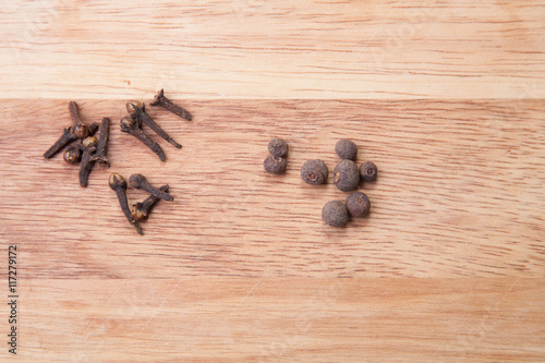Cloves and black pepper on light wooden cutting board