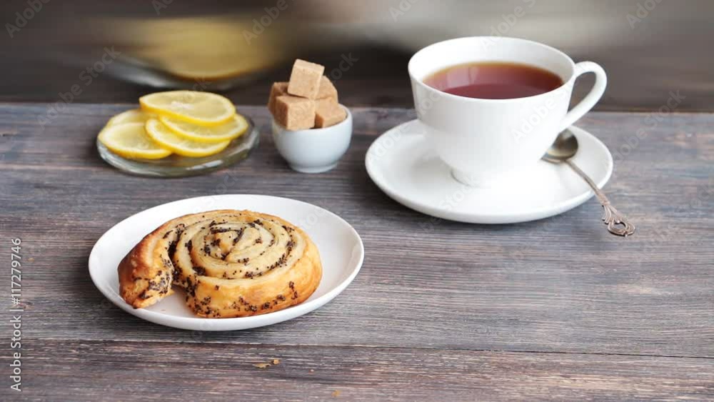 Steaming black tea, brown sugar, lemon and sweet roll cakes with poppy served on a wooden tableagainst steel kitchen background
Steaming black tea, brown sugar, lemon and sweet roll cakes with poppy served on a wooden tableagainst steel kitchen background