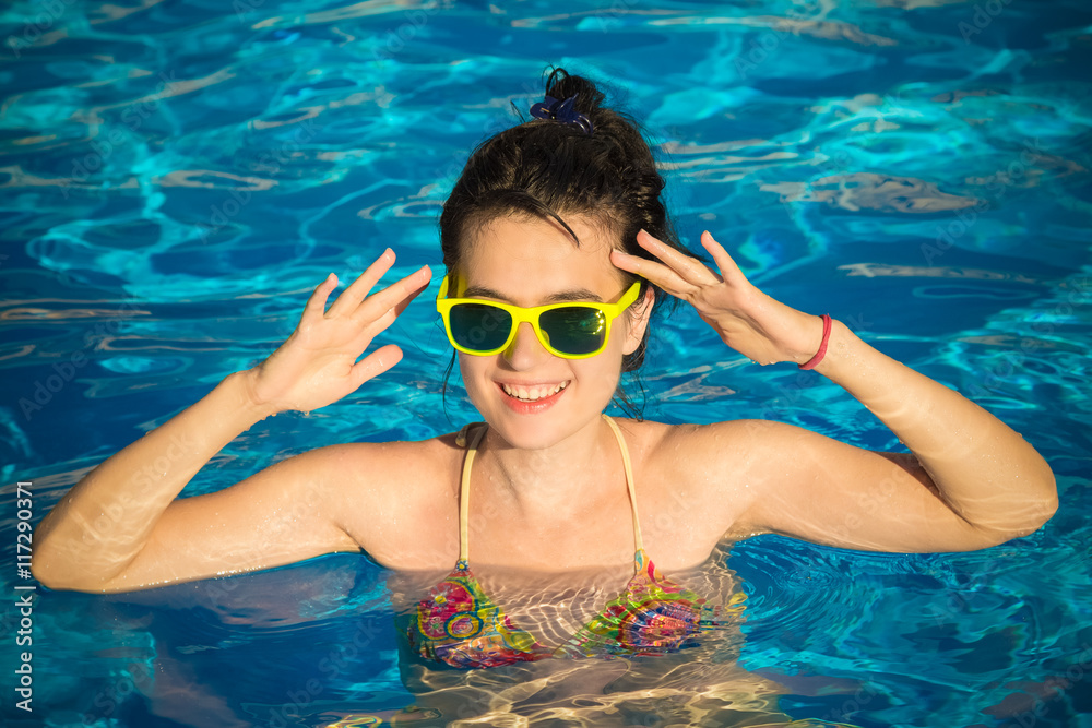 Portrait of young beautiful female wearing sunglasses in the swimming pool. Vacation and summer season concepts. 