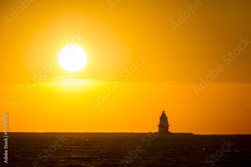 The sun rises behind a silhoetted lighthouse in the Atlantic Ocean. photo