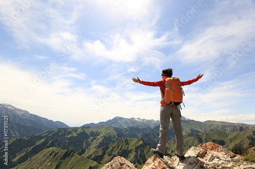 cheering successful woman backpacker open arms on mountain peak