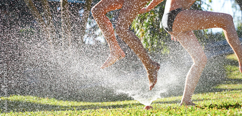 Young girls playing jumping in a garden water lawn sprinkler