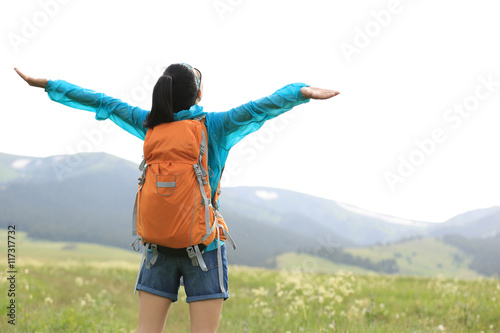 cheering young woman hiker open arms in grassland