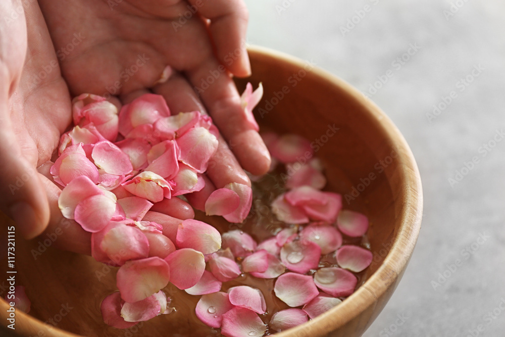Hands in wooden bowl with petals and water