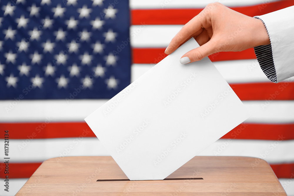 Fototapeta premium Hand putting down voting paper into a ballot box on American flag background