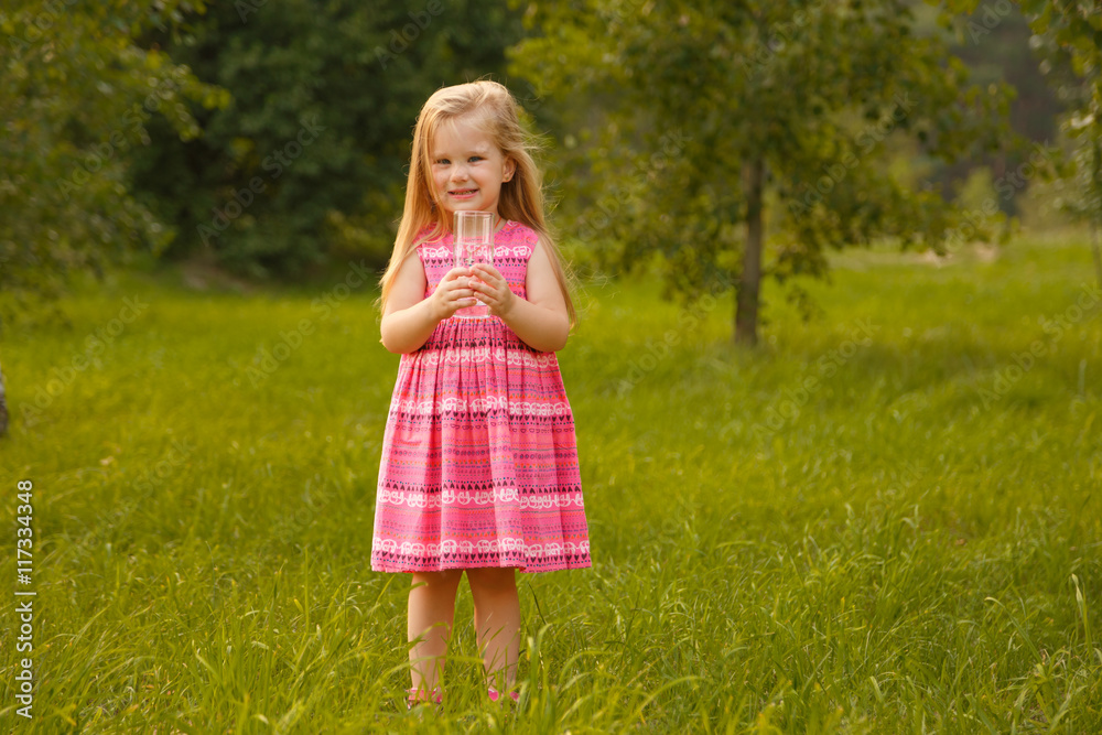 Child holding glass water. Girl in pink dress in summer Child holding glass water. Girl in pink dress in summer
