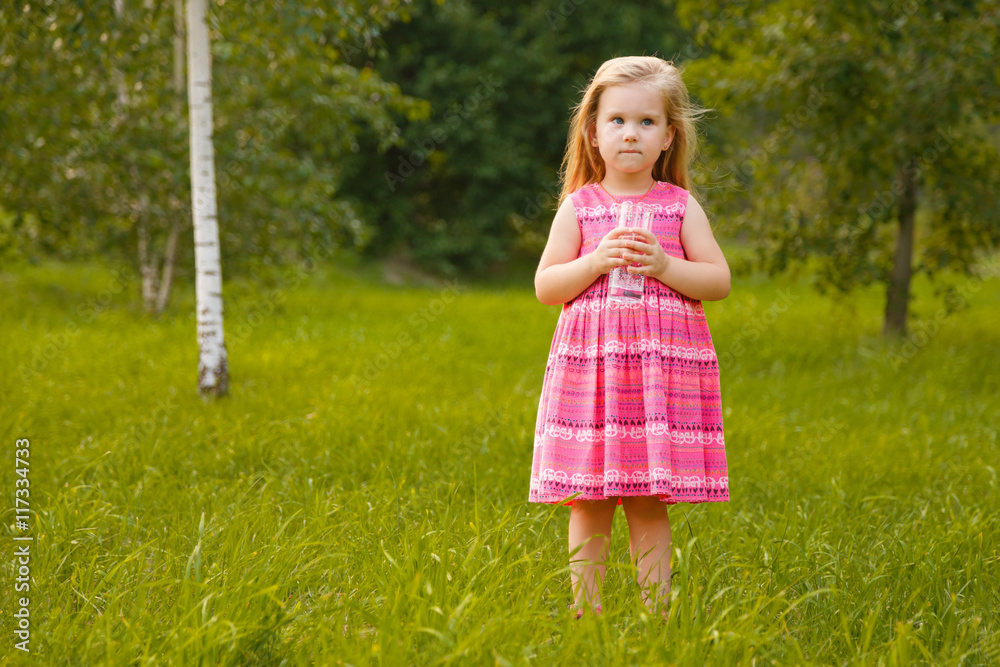 Child holding glass water. Girl in pink dress in summer Child holding glass water. Girl in pink dress in summer