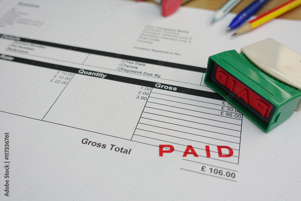 Person Hand Holding Rubber Stamp Over Red Paid Stamp On Invoice Person Hand Holding Rubber Stamp Over Red Paid Stamp On Invoice