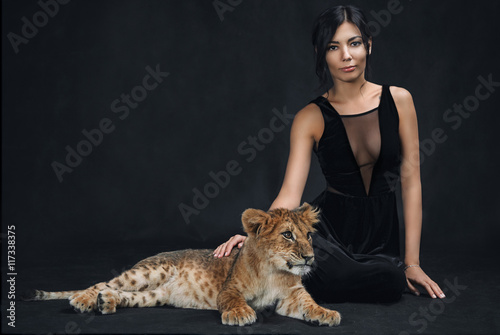Fotografi Beautiful girl playing with a lion cub on a black background
