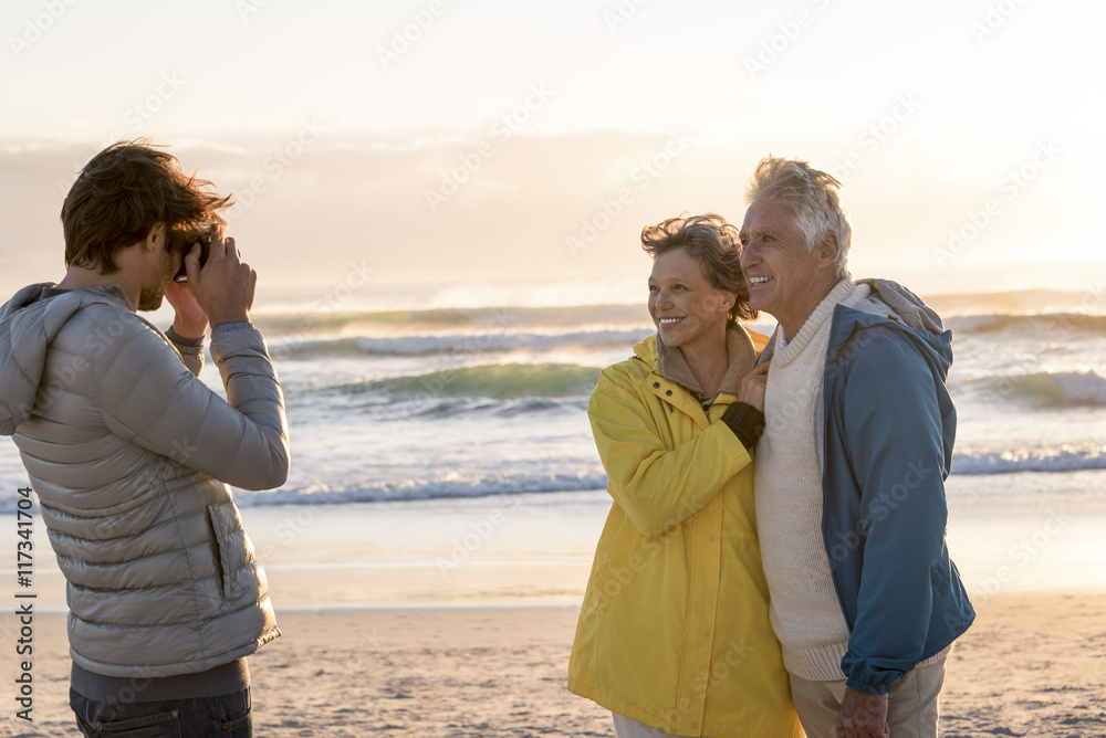 Young man taking a picture of his parents with camera on the beach Young man taking a picture of his parents with camera on the beach