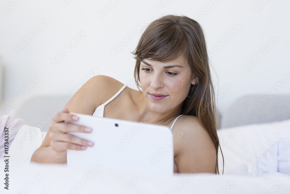 Beautiful young woman lying on the bed using a digital tablet Beautiful young woman lying on the bed using a digital tablet