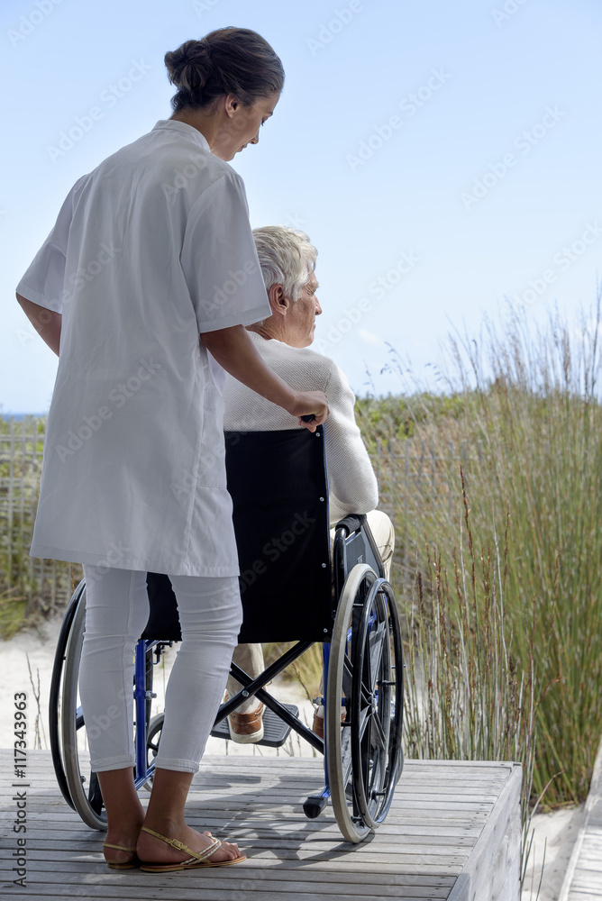 Female nurse assisting senior man in wheelchair outdoors Female nurse assisting senior man in wheelchair outdoors