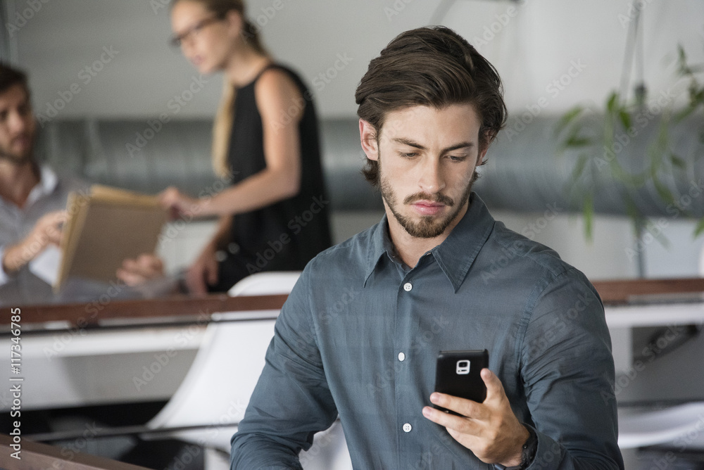 Businessman using a smart phone with his colleagues in the background Businessman using a smart phone with his colleagues in the background