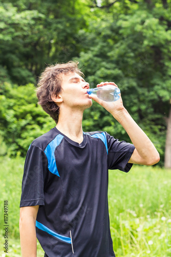 Sport man drinking water from a bottle. Cold drink after outdoor fitness.