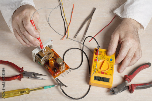 Hand of electrician with multimeter probe at  electrical switchgear cabinet. Engineering tools