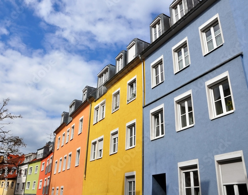 Street with old residential multistory houses of yellow, orange, blue colors in perspective against the blue sky. Lookup.