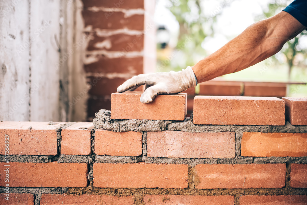 industrial bricklayer worker placing bricks on cement while building exterior walls, industry details - obrazy, fototapety, plakaty 