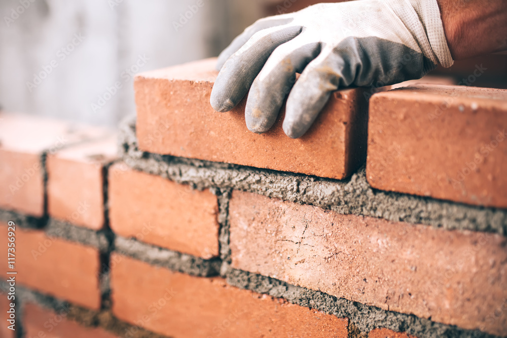 Fototapeta Close up of industrial bricklayer installing bricks on construction site