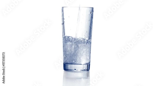 Filling empty glass with carbonated water, dropping ice cubes. Bubbles come out. Close up, extreme close up. 4K Ultra HD.
