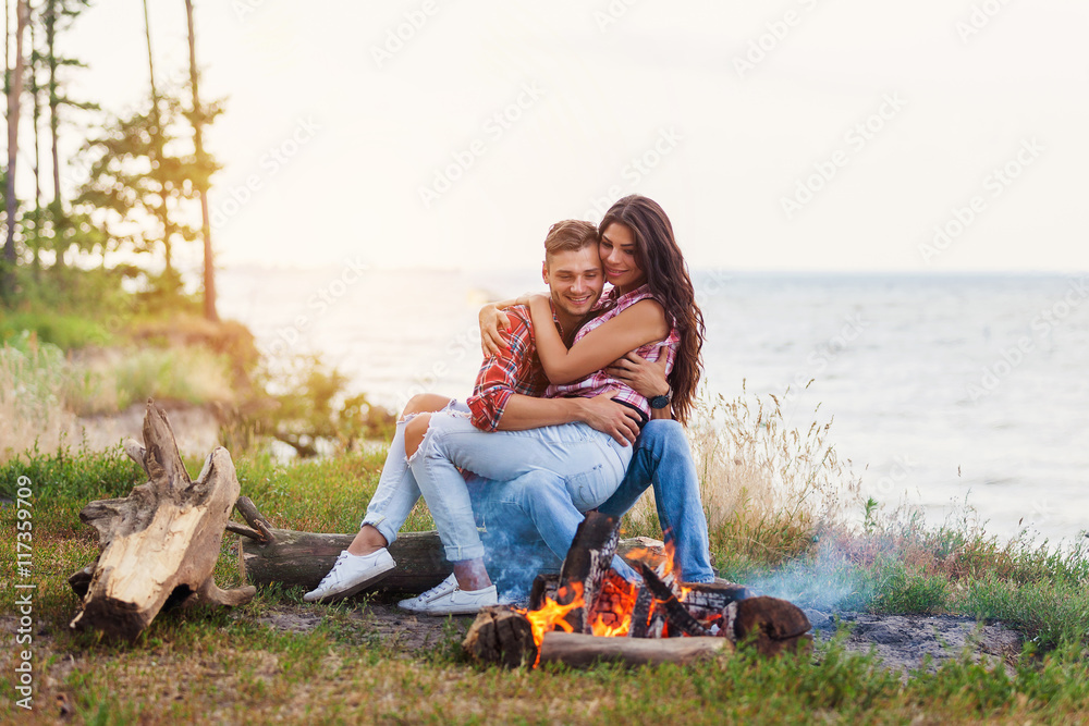 friendship, happiness, summer vacation, holidays and people concept - close up of couple sitting near fire on beach