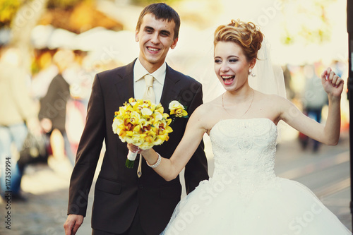 Laughing newlyweds walk along the street in a sunny day