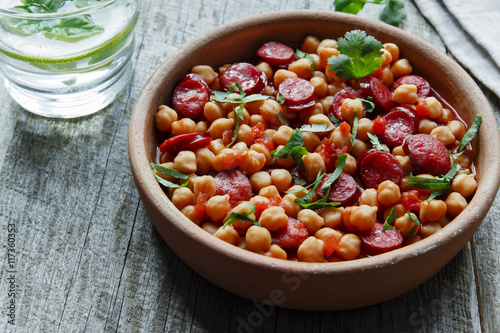 Chickpeas with chorizo in a clay bowl on the table close-up