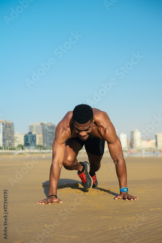 Mountain climbers exercise. Fit man warming up before running at the beach. Black athlete on hiit cardio outdoor workout.