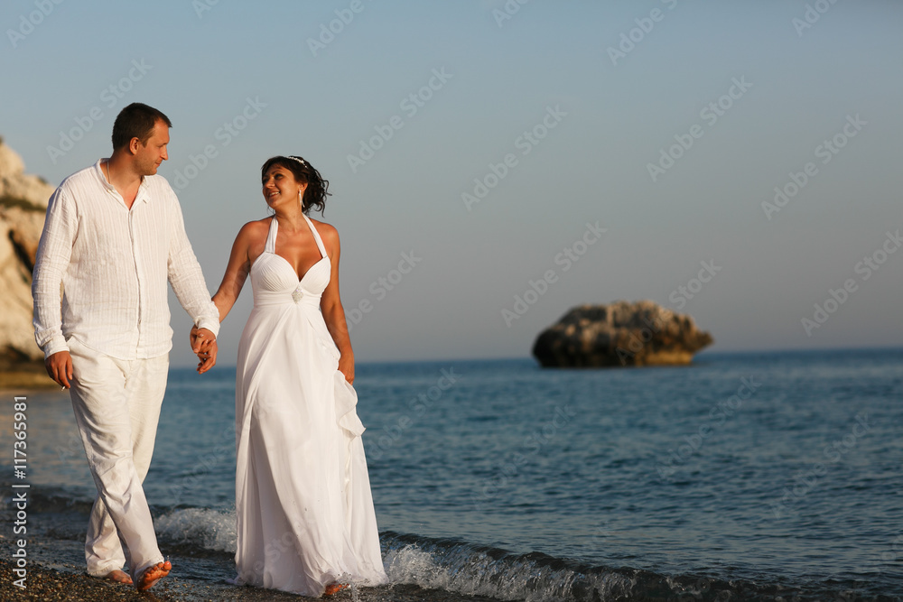 Tanned wedding couple walks along the blue calm sea Tanned wedding couple walks along the blue calm sea