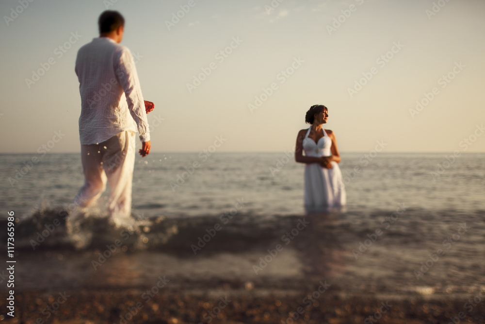 Groom walks to a bride while she enjoys a sunset standing in the
