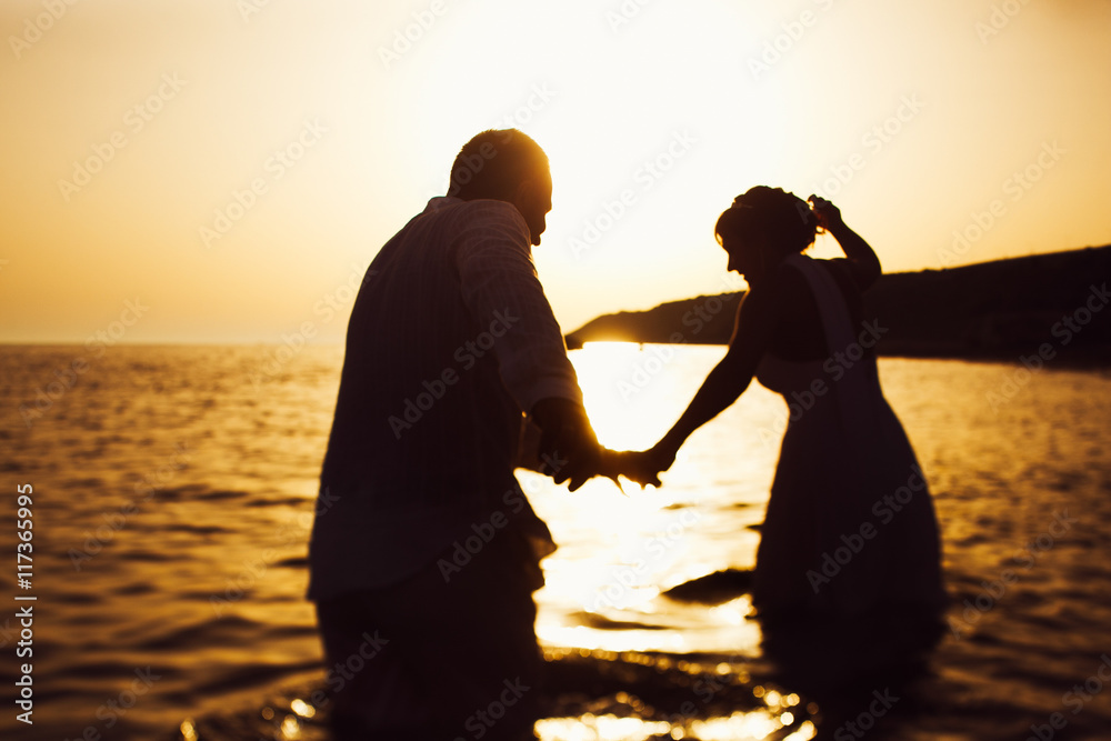 Bride and groom walk in the water to the sunset