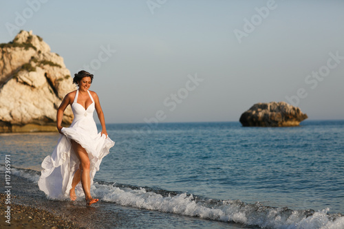 Bride raises her dress up walking in the sea water
