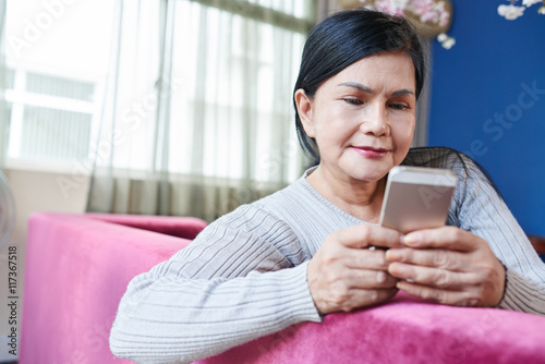 Pretty senior woman sitting on sofa and text messaging