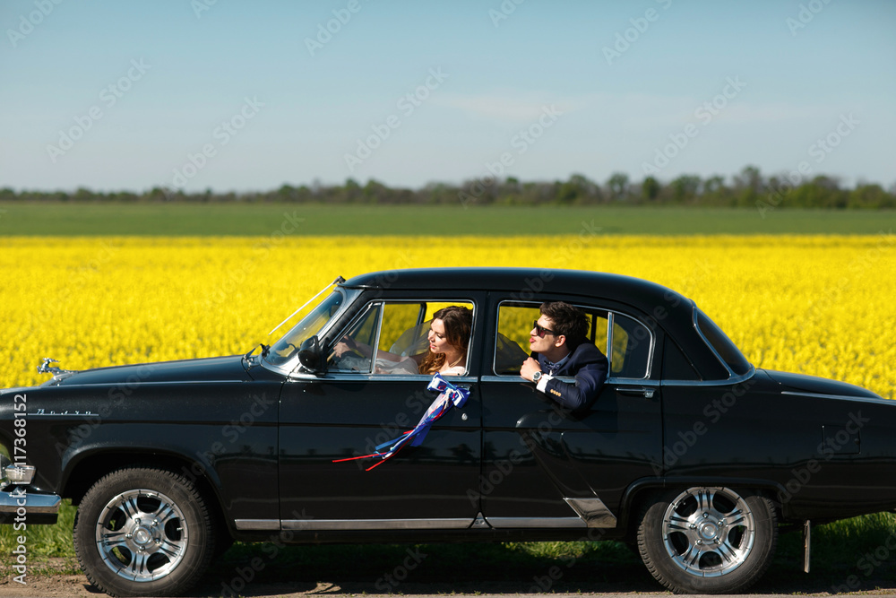 Groom tries to reach a bride from the back seat of an old car Groom tries to reach a bride from the back seat of an old car