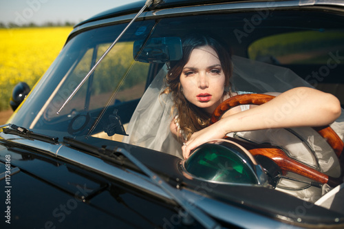 Stunning bride looks through the car's window leaning on a wheel © IVASHstudio