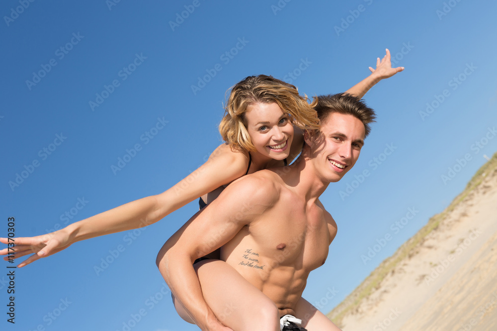 happy young couple on the beach on a piggy back ride happy young couple on the beach on a piggy back ride