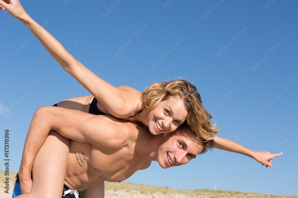 Naklejka premium happy young couple on the beach on a piggy back ride