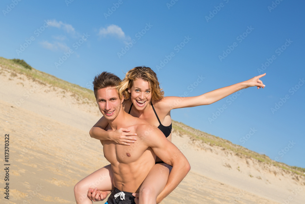 happy young couple on the beach on a piggy back ride happy young couple on the beach on a piggy back ride
