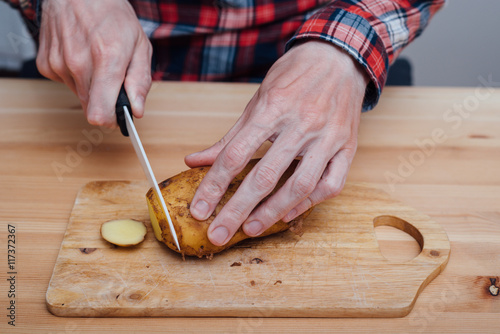 Man hands slicing fresh potato by ceramic knife