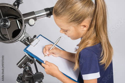 Girl astronomer writes on a sheet of paper of a starry sky with your telescope