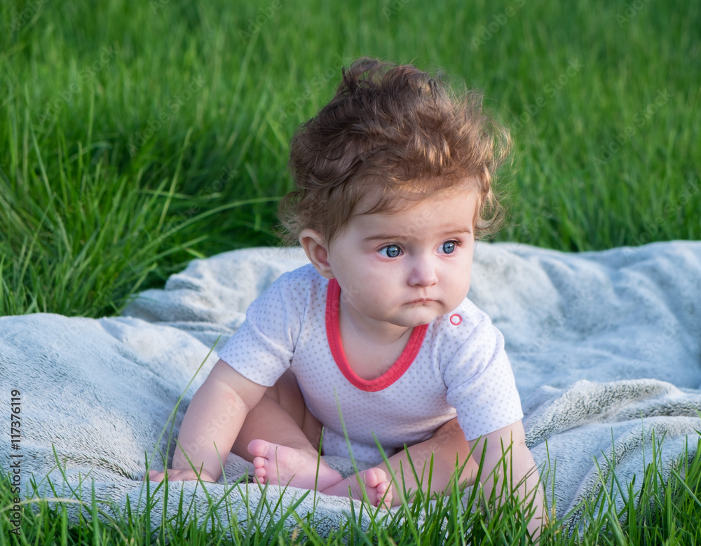 Little girl (six months old) with beautiful blue eyes is sitting on the green grass in the park. Little girl (six months old) with beautiful blue eyes is sitting on the green grass in the park.